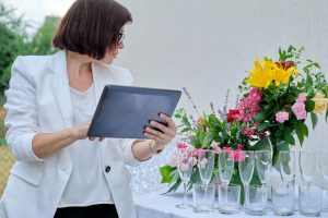 uma profissional envolvida no planejamento de eventos, concentrada enquanto analisa informações em um tablet diante de uma mesa elegantemente preparada.