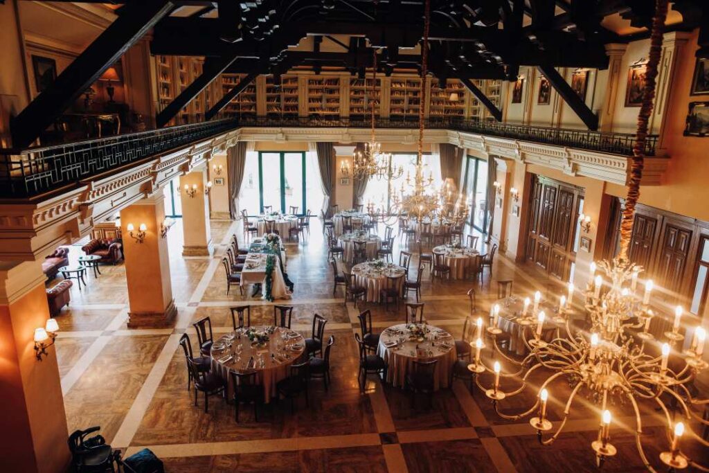 A imagem retrata um elegante espaço de festa, com atmosfera clássica e refinada. O ambiente conta com lustres imponentes, mobiliário sofisticado e um pé-direito alto que valoriza ainda mais a arquitetura tradicional do local. 