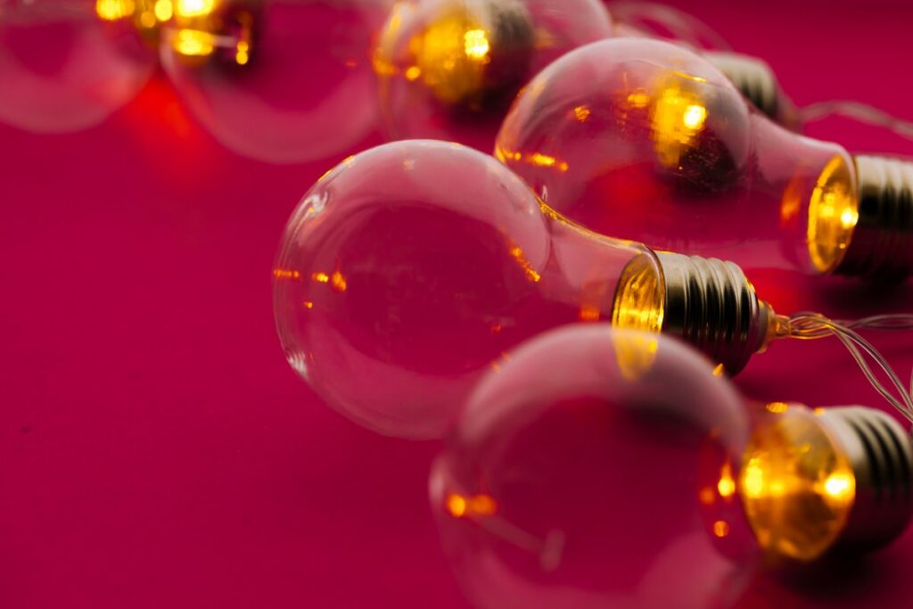 Como um organizador de eventos transforma ideias em experiências inesquecíveis? Nesta imagem vibrante, diversas lâmpadas douradas, levemente iluminadas, estão dispostas sobre um fundo pink intenso, transmitindo uma sensação de criatividade e inspiração.