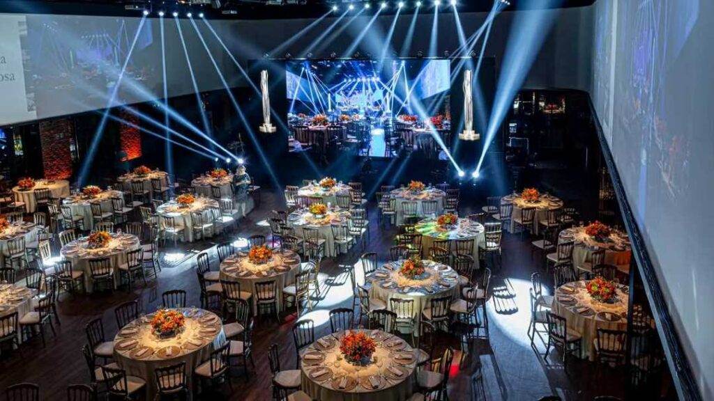 Imagem de um salão amplo e sofisticado preparado para um evento corporativo de grande porte. A decoração é elegante e organizada pela organizadora de eventos Bisutti.