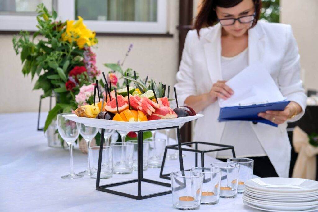 O que nenhuma organizadora de eventos pode esquecer? uma profissional envolvida no planejamento de eventos, concentrada enquanto analisa informações em um tablet diante de uma mesa elegantemente preparada.